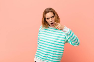 Genç sarışın kadın, kızgın agresif bir ifadeyle kameraya bakıyor. Düz duvara karşı öfkeli, çılgın bir patron gibi görünüyor.