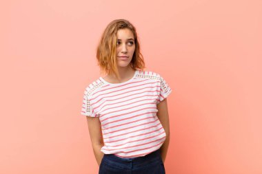 Genç sarışın kadın üzgün, üzgün ya da kızgın ve olumsuz bir tavır takınıyor, düz renk duvarına karşı anlaşmazlık içinde.