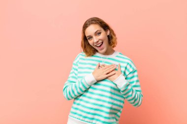 Genç sarışın kadın romantik, mutlu ve aşık, neşeyle gülümsüyor ve düz renkli duvara karşı kalbe yakın el ele tutuşuyor.