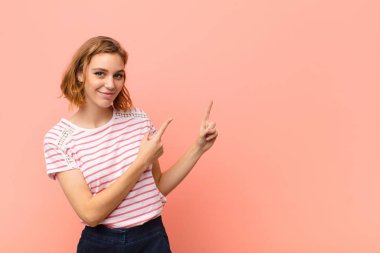Genç sarışın kadın mutlu bir şekilde gülümsüyor ve iki eliyle yukarı ve yana doğru gösteriyor fotokopi uzayında düz renkli duvara karşı nesne gösteriyor.