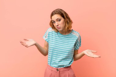 Genç sarışın kadın şaşkın ve şaşkın hissediyor, doğru cevap ya da karardan emin değil, düz renkli duvara karşı bir seçim yapmaya çalışıyor.