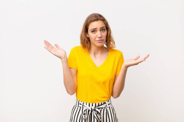 Genç sarışın kadın şaşkın ve şaşkın hissediyor, şüpheci, farklı seçenekleri tartıyor ya da seçiyor düz renkli duvara karşı komik bir ifadeyle