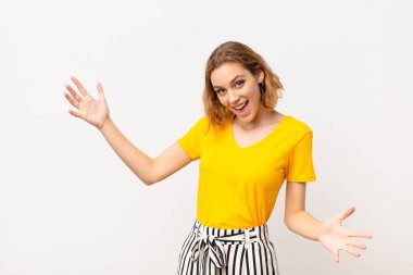 Genç sarışın kadın mutlu, kibirli, gururlu ve kendinden memnun görünüyor. Düz renkli duvara karşı kendini bir numara gibi hissediyor.