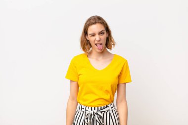 Genç sarışın kadın neşeli, kaygısız, asi tavırlı, şakacı ve dilsiz, düz renkli duvara karşı eğlenen