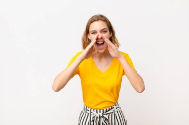 Genç sarışın kadın mutlu, heyecanlı ve pozitif hissediyor. Elleri ağızda, düz duvara karşı bağırıyor.