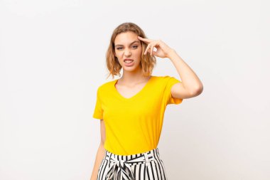 Genç sarışın kadın şaşkın ve şaşkın hissediyor. Deli, deli ya da düz renkli duvara karşı aklını kaçırmış olduğunu gösteriyor.