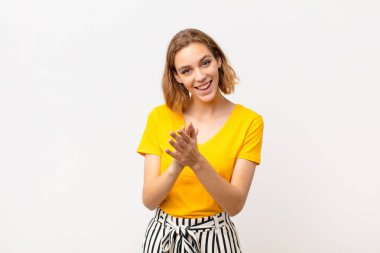 Genç sarışın kadın mutlu ve başarılı hissediyor, gülümsüyor ve alkışlıyor, düz renkli duvara karşı alkış ile tebrik ediyor.