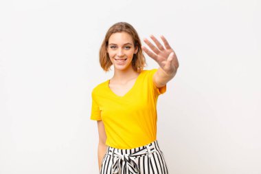 Genç sarışın kadın gülümsüyor ve arkadaş canlısı görünüyor. Dört ya da dört numarayı gösteriyor. Elleri önde, düz renkli duvara doğru sayıyor.