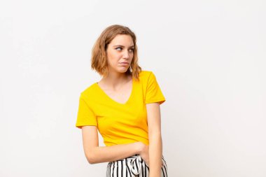 Genç sarışın kadın üzgün, üzgün ya da kızgın ve olumsuz bir tavır takınıyor, düz renk duvarına karşı anlaşmazlık içinde.