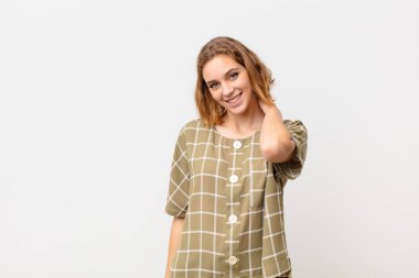 Genç sarışın kadın neşeli ve kendinden emin bir şekilde gülümsüyor. Düz renkli duvara karşı güler gibi gülümsüyor.