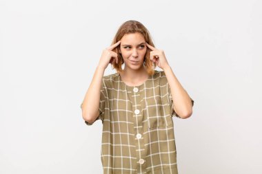 Genç sarışın kadın bir fikre odaklanmış ve kafa yoruyor, düz renk duvarlara karşı bir meydan okuma veya probleme çözüm hayal ediyor.