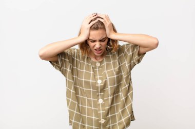 Genç sarışın kadın kendini stresli ve hayal kırıklığına uğramış hissediyor. Yumruk yumruğa, yorgun, mutsuz ve migreni düz renkli duvara dayanmış.