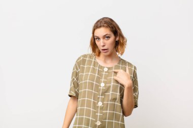 Genç sarışın kadın şaşkın, şaşkın ve güvensiz hissediyor. Kendini gösterip kim olduğumu soruyor. Ben mi? yassı renk duvarına karşı