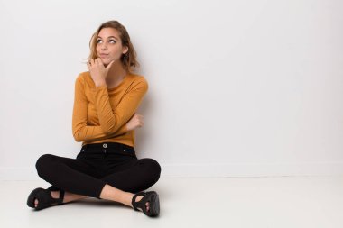 Genç sarışın kadın düşünceli, meraklı ya da hayal kuruyor, hayal kuruyor ve düz renkli duvarlara karşı mekanı kopyalamak istiyor.