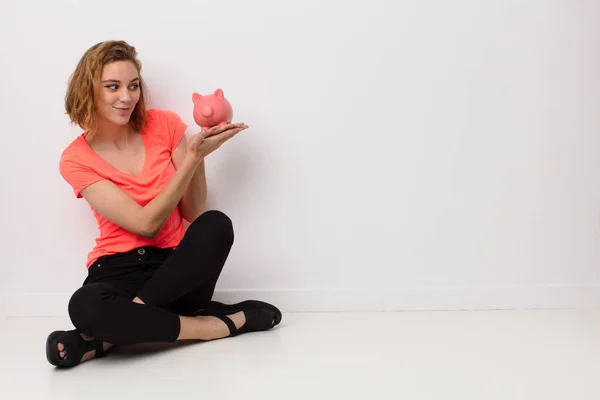 Mujer Rubia Joven Contra Pared Color Plano Con Una Alcancía — Foto de Stock