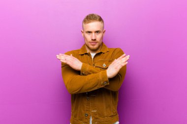 Genç sarışın adam senin bu tavırlarından rahatsız ve bıkkın görünüyor, yeter artık! Eller önde çapraz, mor arka planda durmanı söylüyor.