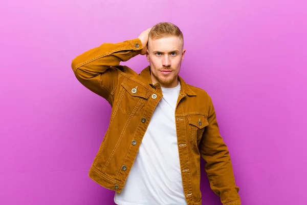 young blonde man panicking over a forgotten deadline, feeling stressed, having to cover up a mess or mistake against purple background