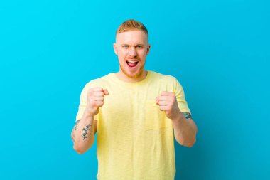 Sarı tişörtlü genç adam sinirli, sinirli, sinirli bakışlı ve yumruklarını sıkmış, öfkeli bir şekilde bağırıyor.