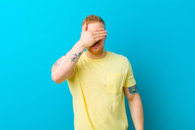 Sarı tişörtlü genç bir adam bir eliyle gözlerini kapatıyor korkmuş ya da endişeli, merak ediyor ya da körü körüne bir sürpriz bekliyor.