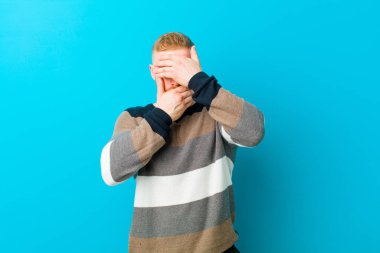 Genç sarışın adam kameraya hayır diyen iki eliyle yüzünü kapatıyor! Resimler reddediliyor ya da mavi arkaplana karşı resimler yasaklanıyor