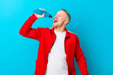 Mavi arka planda spor kıyafetleri giyen genç sarışın adam. fitness konsepti