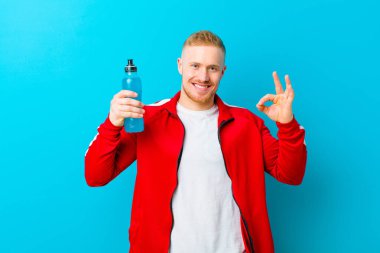 Mavi arka planda spor kıyafetleri giyen genç sarışın adam. fitness konsepti