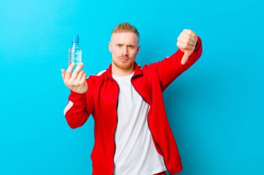 Mavi arka planda spor giysileri giyen, su şişeli genç sarışın bir adam. fitness konsepti