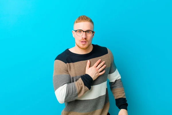 Joven Hombre Rubio Sintiéndose Sorprendido Sorprendido Sonriendo Tomando Mano Corazón —  Fotos de Stock