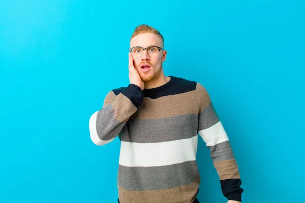 Joven Hombre Rubio Siente Sorprendido Asombrado Sosteniendo Cara Mano Incredulidad —  Fotos de Stock