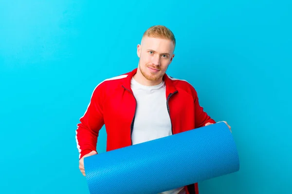 young blonde man wearing sports clothes  against blue background. fitness concept