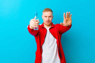 Mavi arka planda spor giysileri giyen, su şişeli genç sarışın bir adam. fitness konsepti