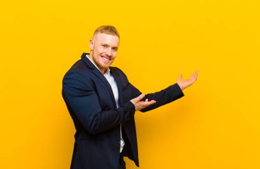 Genç sarışın işadamı gururla ve güvenle gülümsüyor, mutlu ve tatmin olmuş hissediyor ve fotokopi alanında bir konsept gösteriyor.