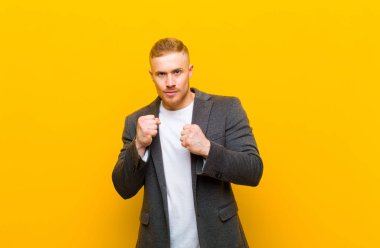 Genç sarışın iş adamı kendinden emin, sinirli, güçlü ve agresif görünüyor. Yumrukları boks pozisyonunda dövüşmeye hazır.