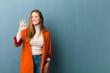 Genç ve güzel bir kadın kendini başarılı ve tatmin olmuş hissediyor, ağzı açık gülümsüyor, elle işaret veriyor.