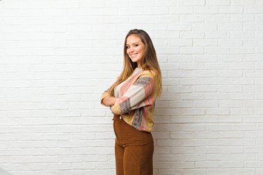 Genç ve güzel bir kadın kameraya çapraz kollarıyla gülümsüyor ve mutlu, kendinden emin, tatmin olmuş bir ifade, yan bakış.