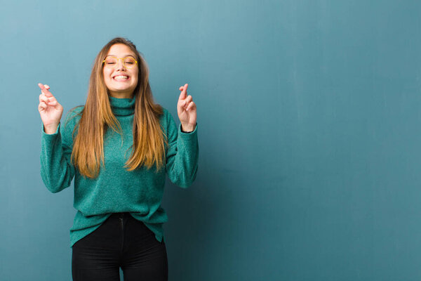 young pretty woman smiling and anxiously crossing both fingers, feeling worried and wishing or hoping for good luck