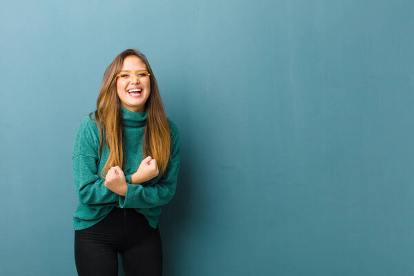 young pretty woman smiling cheerfully and celebrating, with fists clenched and arms crossed, feeling happy and positive