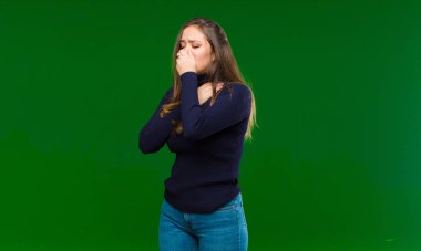 Gırtlağı ağrıyan ve grip belirtileri gösteren, ağzı yeşil arka planda öksüren genç ve güzel bir kadın.