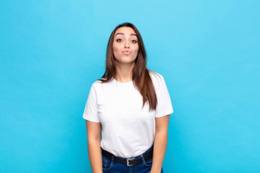 Genç, güzel bir kadın dudaklarını birbirine bastırıyor. Sevimli, eğlenceli, mutlu, sevimli bir yüz ifadesiyle. Mavi duvara bir öpücük yolluyor.