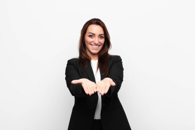 Genç ve güzel iş kadını mutlu bir şekilde gülümsüyor. Beyaz duvara karşı bir nesne ya da konsept sunuyor ve sunuyor.