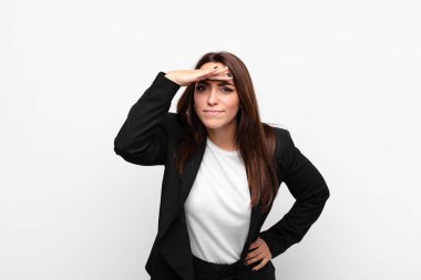 Genç ve güzel iş kadını şaşkınlık ve şaşkınlık içinde bakıyor, el üstünde uzak bakıyor, beyaz duvarın karşısında izliyor ya da arıyor