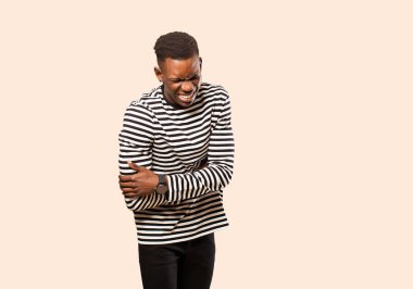 Genç Afrikalı Amerikalı siyahi adam endişeli, hasta, hasta ve mutsuz hissediyor, bej duvarda acı veren bir mide ağrısı ya da grip geçiriyor.