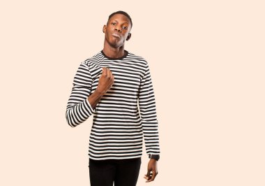 Genç Afrikalı Amerikalı siyah adam kibirli, başarılı, pozitif ve gururlu görünüyor, bej rengi duvara karşı kendini işaret ediyor.