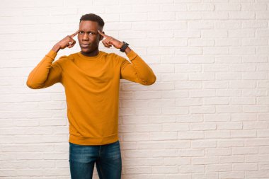 young african american black man feeling confused or doubting, concentrating on an idea, thinking hard, looking to copy space on side against brick wall