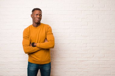young african american black man doubting or thinking, biting lip and feeling insecure and nervous, looking to copy space on the side against brick wall