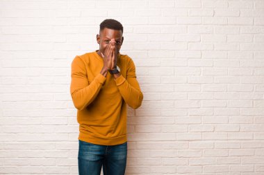 young african american black man looking happy, cheerful, lucky and surprised covering mouth with both hands against brick wall