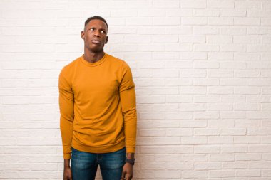 young african american black man with a worried, confused, clueless expression, looking up to copy space, doubting against brick wall