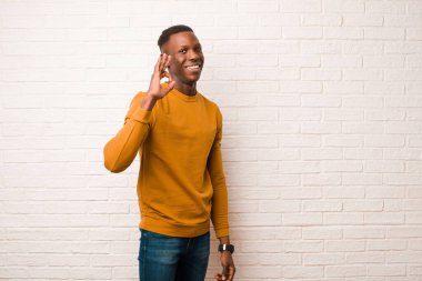 young african american black man feeling happy, relaxed and satisfied, showing approval with okay gesture, smiling against brick wall