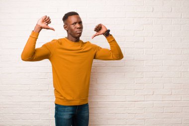 Genç Afro-Amerikan siyahi adam üzgün, hayal kırıklığına uğramış ya da kızgın görünüyor, anlaşmazlık içinde parmaklarını gösteriyor, tuğla duvara karşı hayal kırıklığına uğramış hissediyor