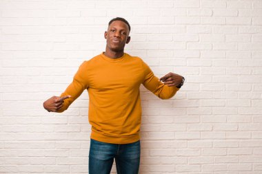 Genç Afrikalı Amerikalı siyah adam gururlu, kibirli, mutlu, şaşırmış ve tatmin olmuş görünüyor, kendini işaret ediyor, tuğla duvara karşı bir kazanan gibi hissediyor.